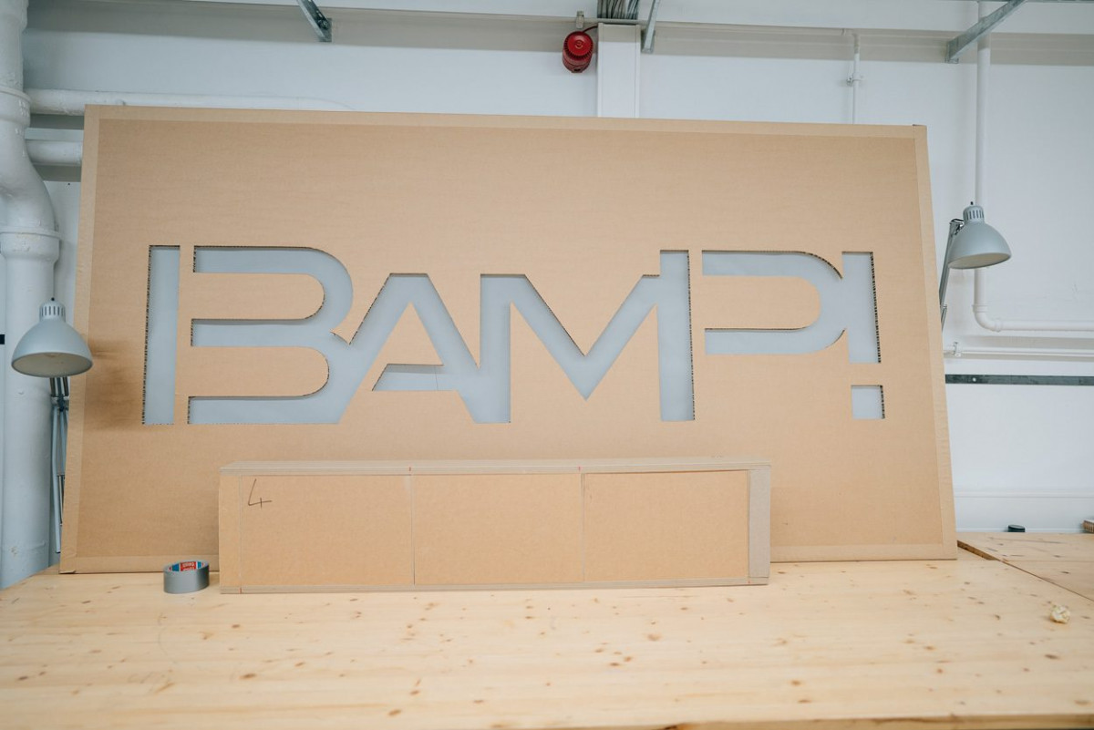 Der Name des Schwerpunkts "BAMP!" in einen große Pappwand gestanzt.