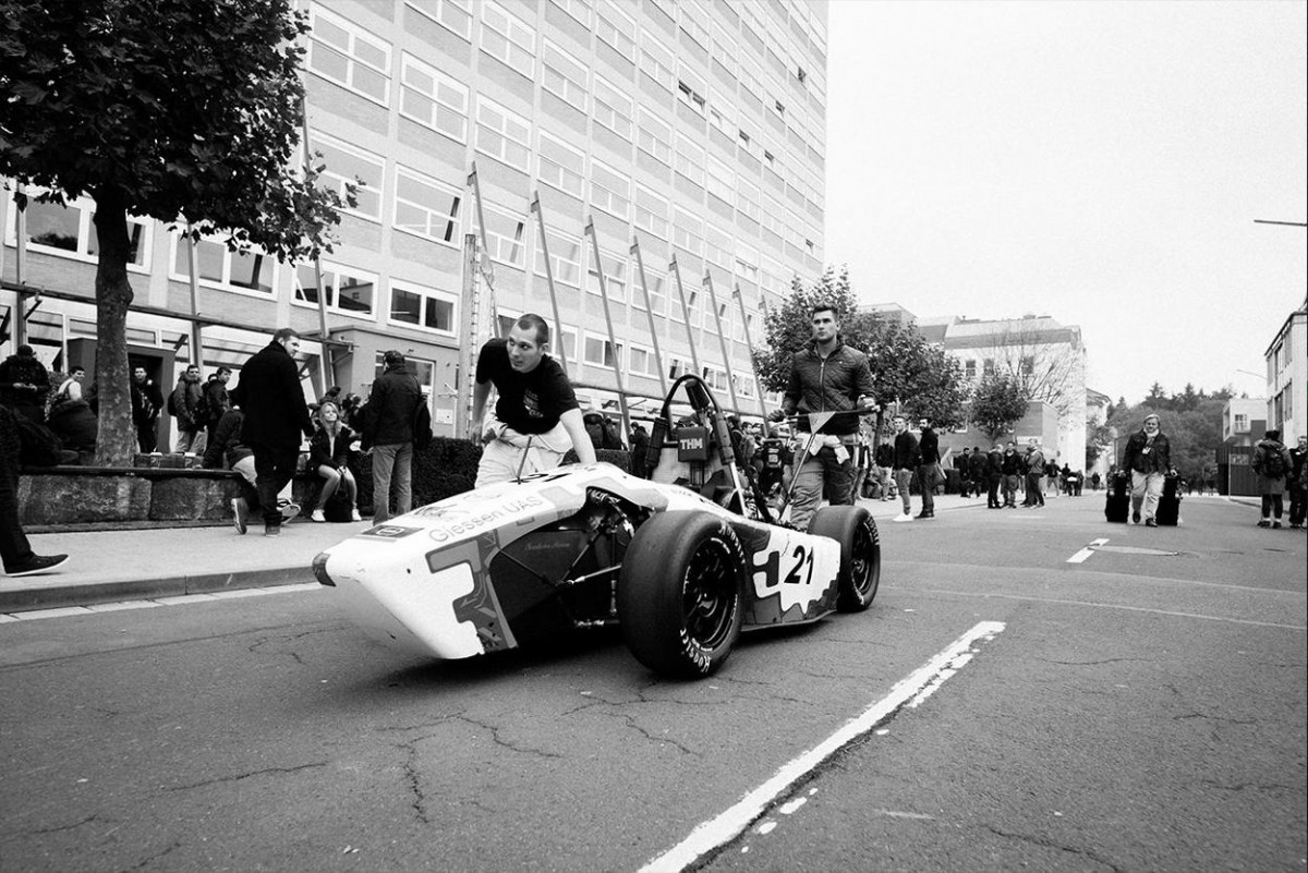 Zwei Mitglieder des Racing Teams schieben einen Rennwagen über den Campus der Technischen Hochschule Mittelhessen