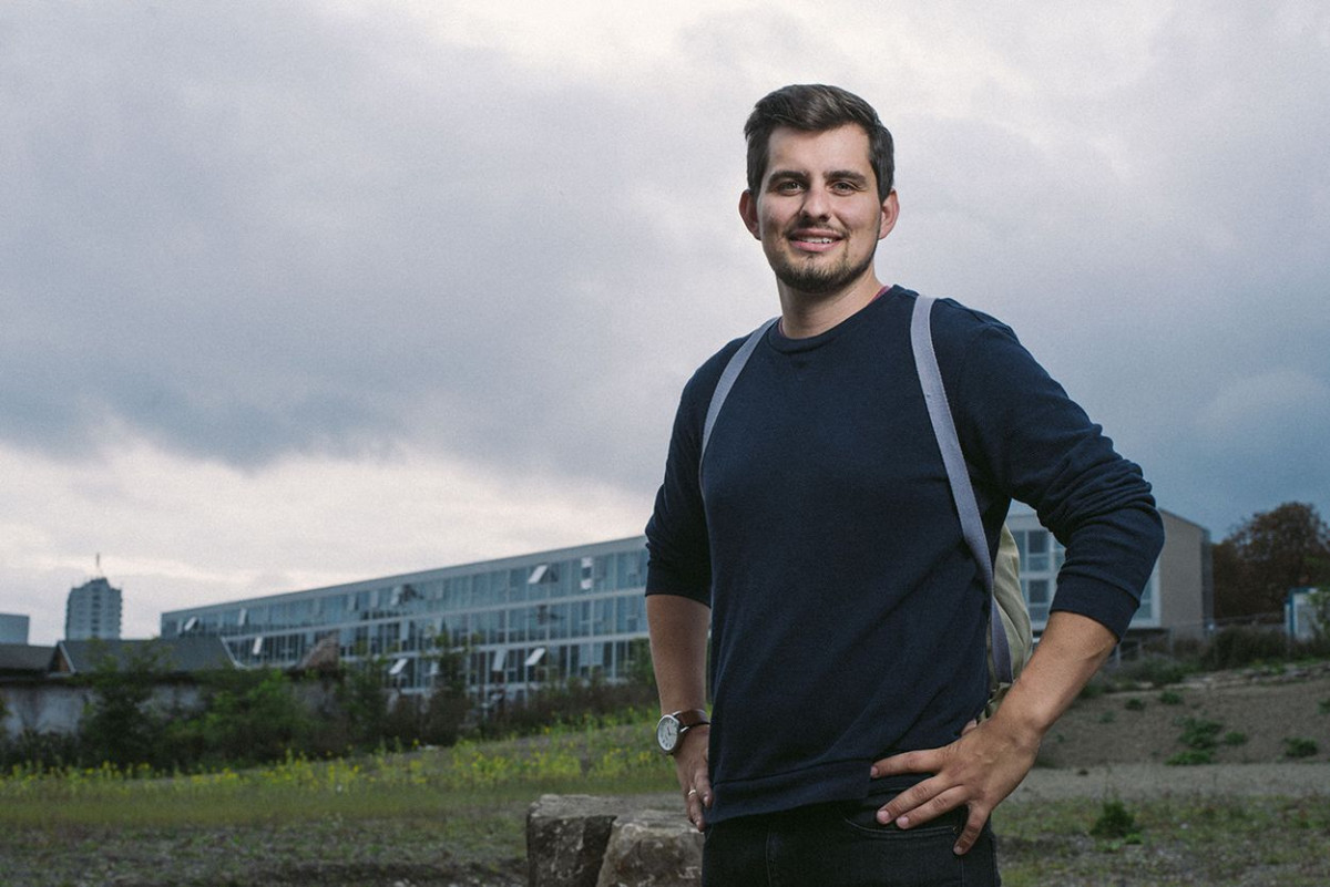 Ein junger Mann steht im Feld nahe der Universität Kassel und trägt eine Amuza Bag