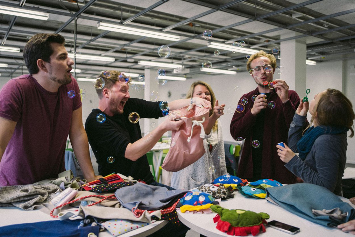 Eine ausgelassene Gruppe Studierender macht Seifenblasen, auf dem Tisch liegen gefertigte Taschen