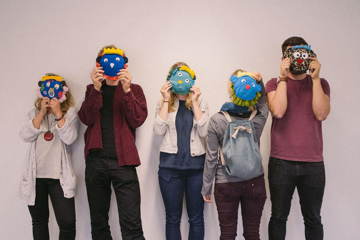Eine Gruppe Studierender hält sich aus Stoff gefertigte Gesichter vors Gesicht