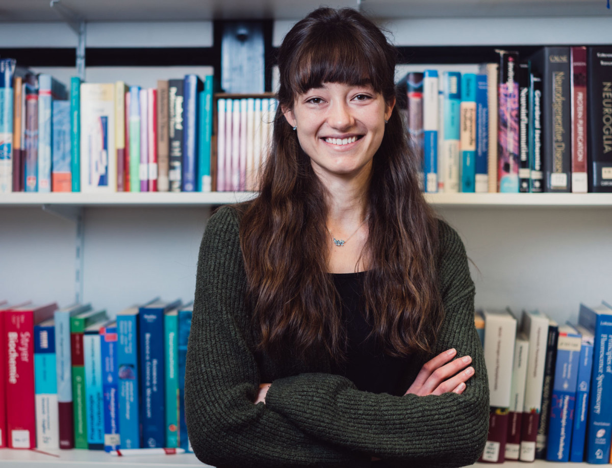 Katharina Becker von der Philipps-Universität Marburg steht vor einem Regal mit Fachliteratur.