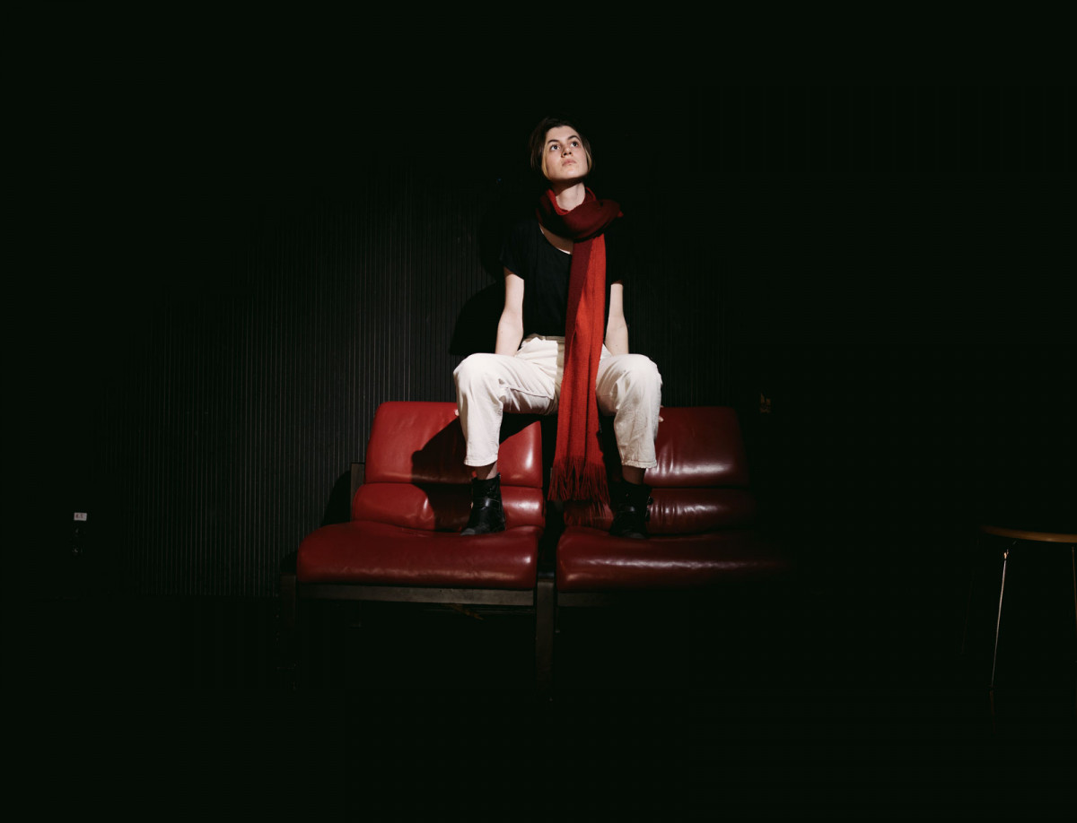 Schauspielstudentin Fenna sitzt auf der Lehne von zwei roten Ledersitzen.