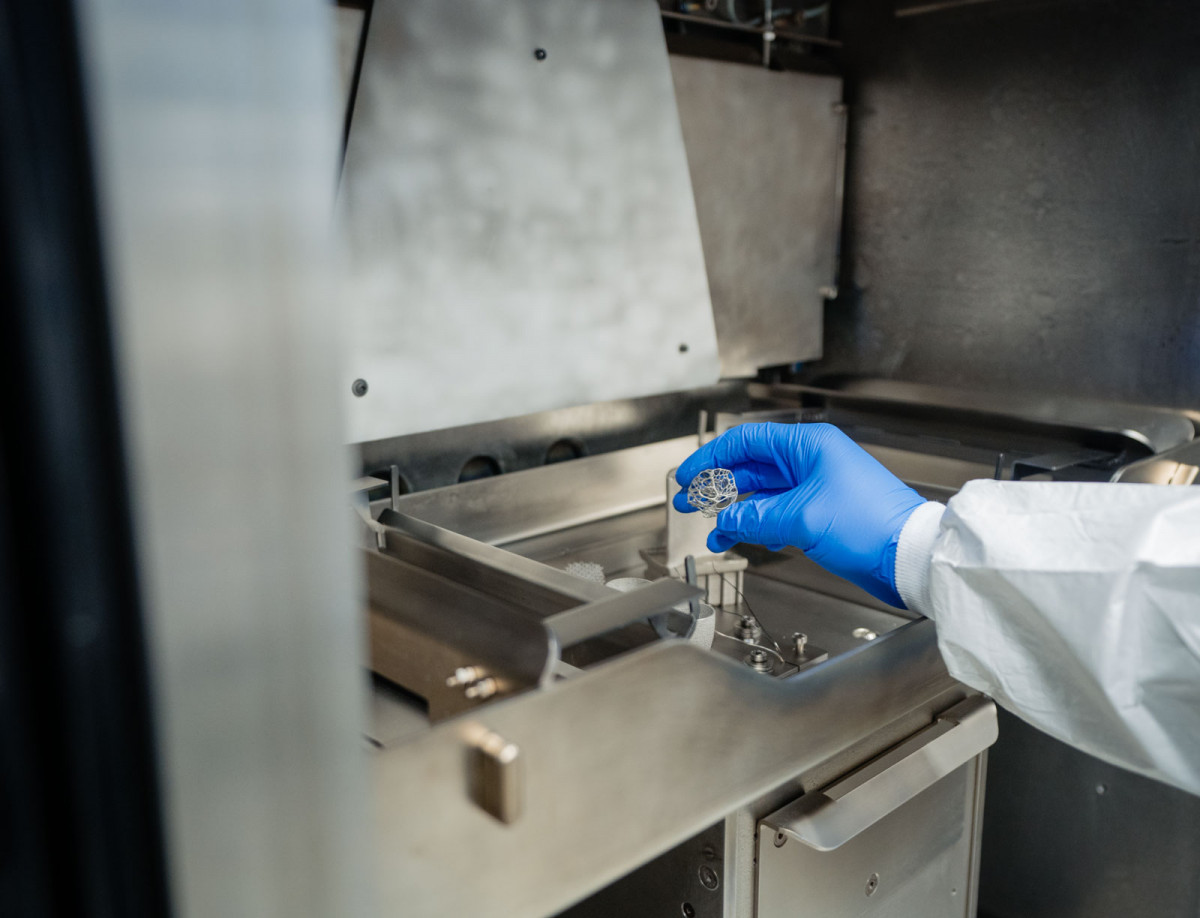 Ein Student nimmt ein Metallteil aus einem Metalldrucker.