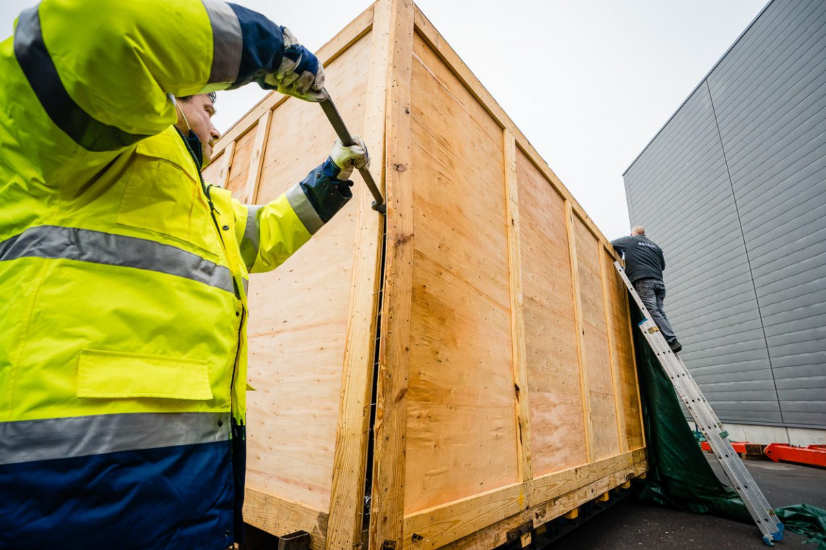 Ein Arbeiter hebelt die Holzkiste auf, in der die neue Maschine geliefert wurde.