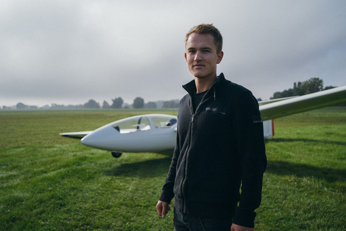 Ein junger Mann steht vor einem gelandeten Segelflugzeug