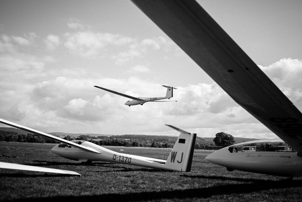 Ein Segelflugzeug fliegt am Himmel, während weitere am Boden stehen