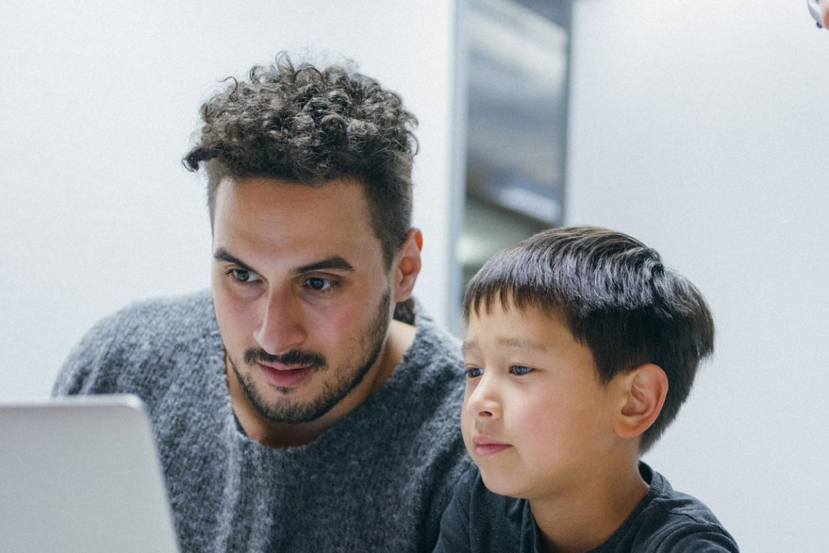 Ein Mann und ein Junge schauen interessiert auf das Display eines Laptops
