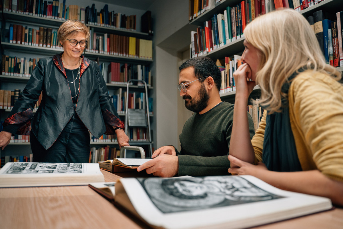 Prof. Dr. Böhlendorf-Arslan in der Bibliothek mit den Studierenden Alieda Halbersmah und Hüseyin Çinarlik.