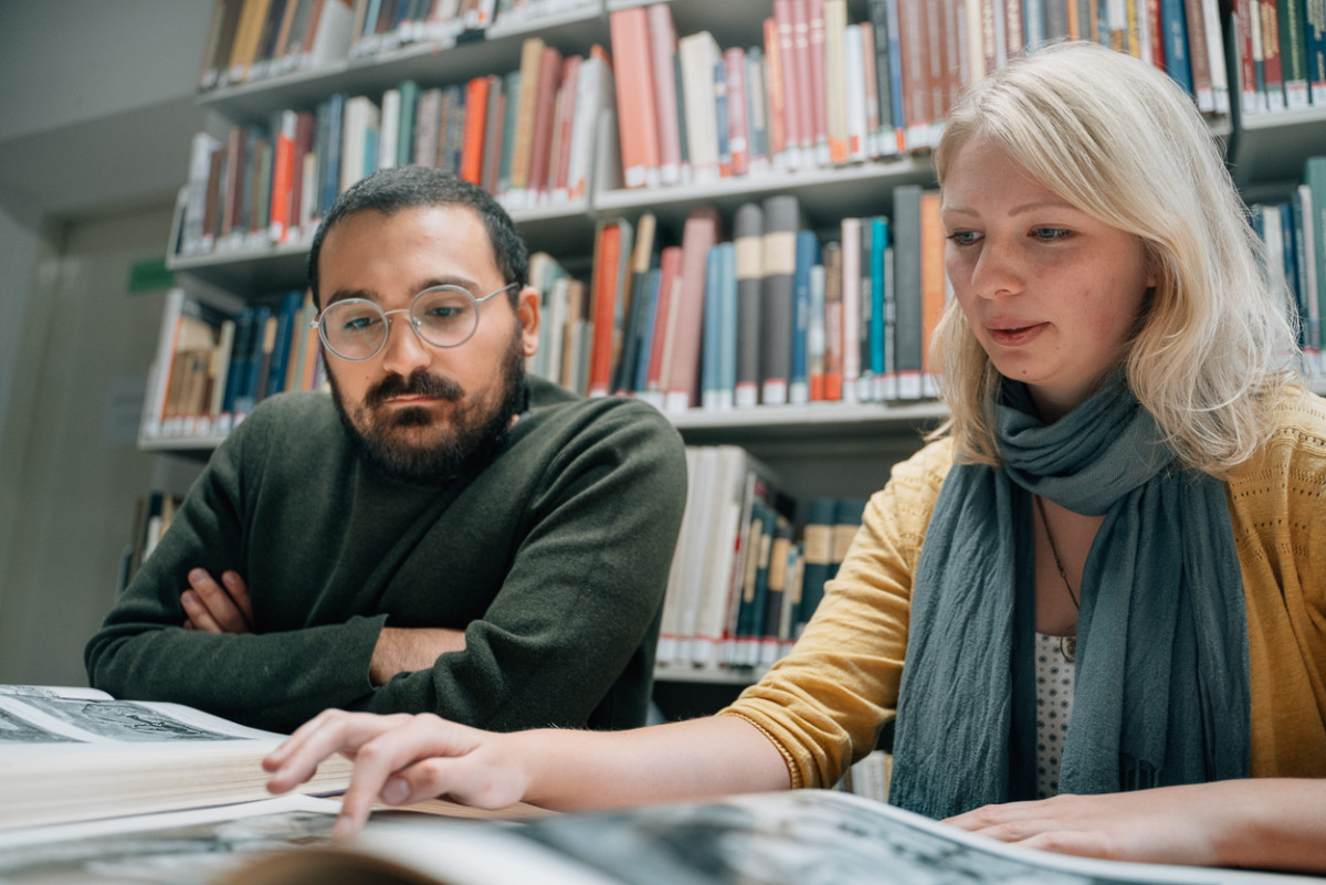 Alieda Halbersmah und Hüseyin Çinarlik betrachten historische Bücher in der Bibliothek.